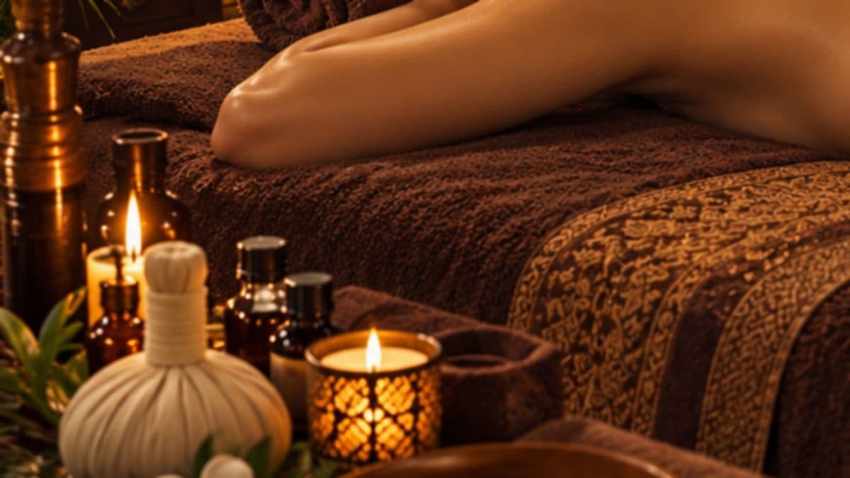 Túi chườm thảo dược, chai tinh dầu và ánh nến cạnh giường phủ khăn nâu