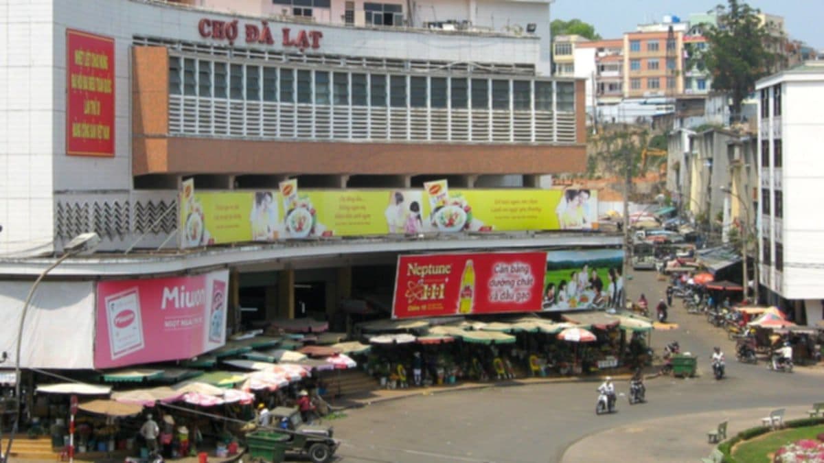 Da Lat Market by day: the market building with umbrella-shaded stalls and motorbikes on the street in front
